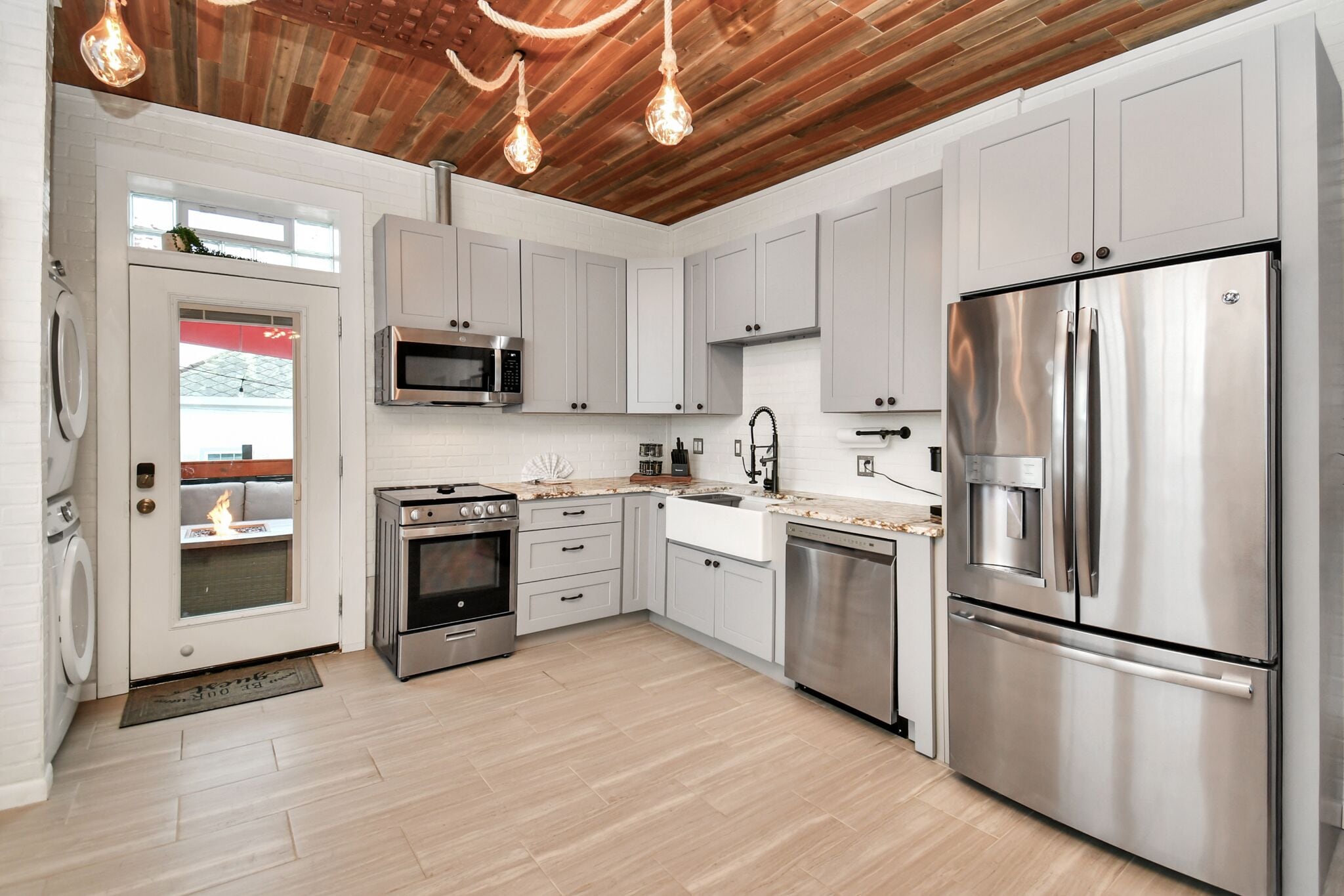 A modern kitchen with stainless steel appliances, white cabinetry, and a wooden ceiling.