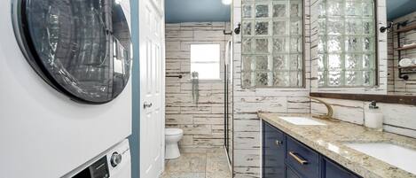 A compact laundry room with a front-loading washer and dryer, a white toilet, and a large window with frosted glass panels.