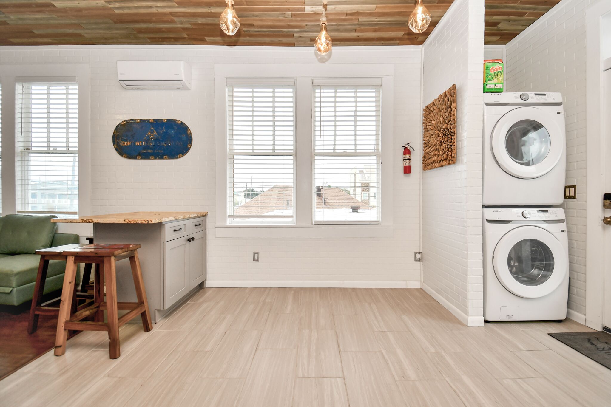 A laundry room with two washing machines, a wooden stool, a green couch, and a window with blinds.