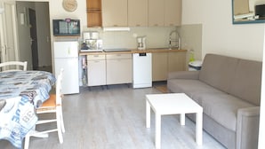 Ett kompakt bostadsutrymme med ett litet kök, en matplats med bord och stolar samt en soffa.