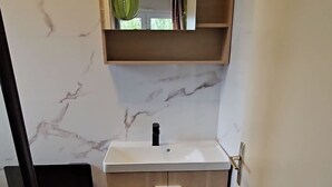Ett modernt badrum med en väggbeklädnad av marmor, ett badrumsskåp i trä och ett litet fönster med utsikt.