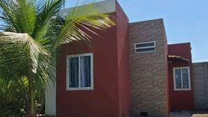 Ein modernes Haus mit roter Fassade, einem Pflasterweg und einer Palme.