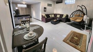 Ein modernes Wohnzimmer mit Essbereich, einer Couch, einem Hängesessel und einer Küche im Hintergrund.
