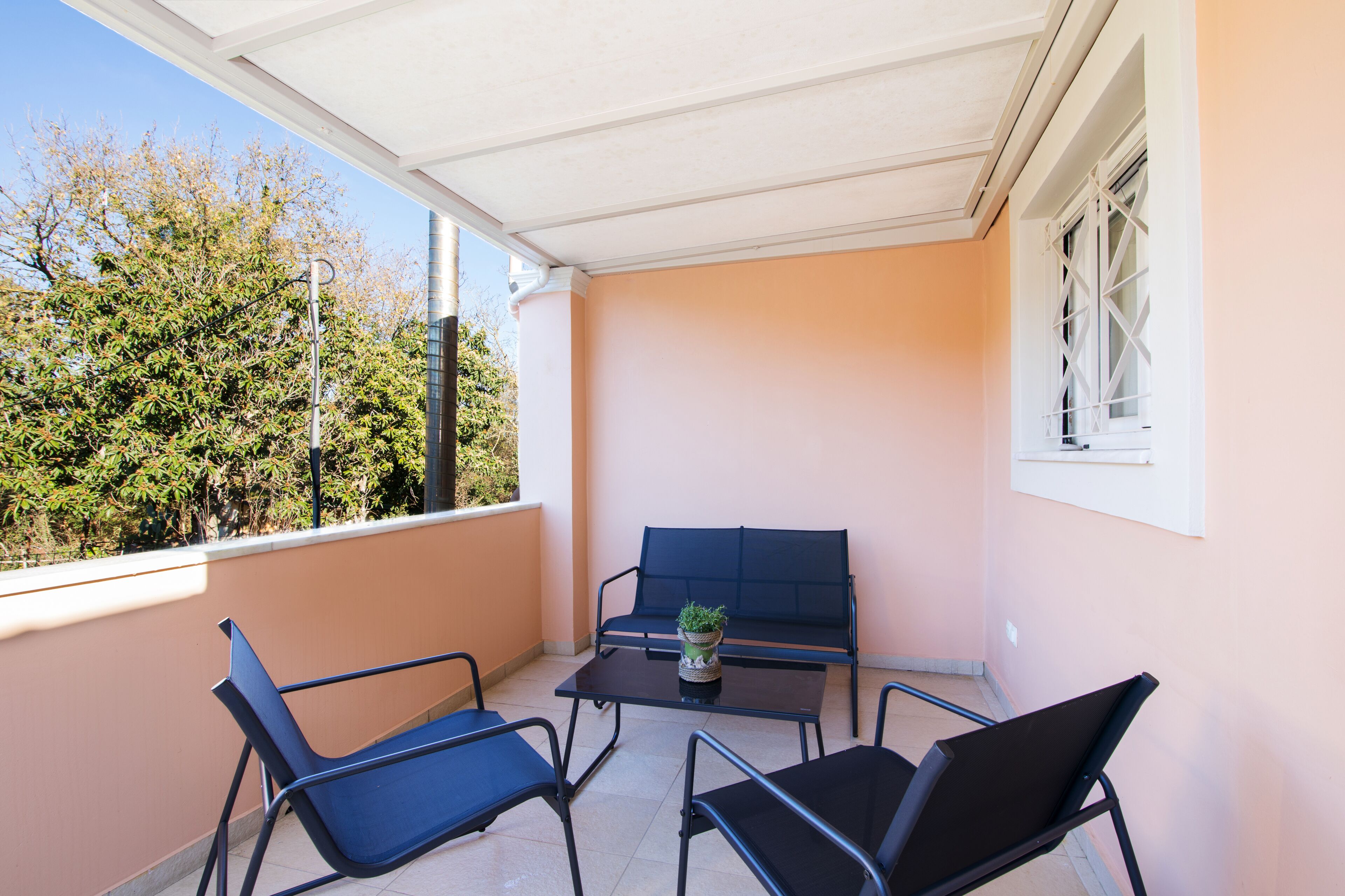 A balcony with a table, two chairs, a bench, and a potted plant.
