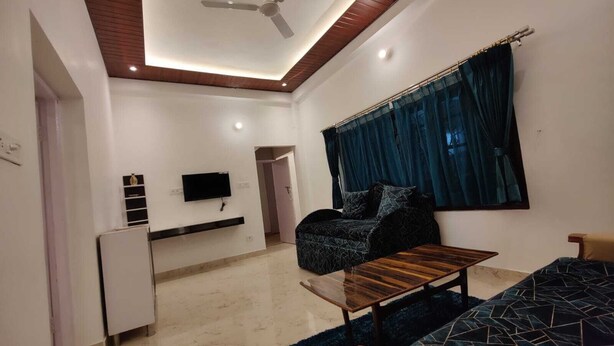 Una sala moderna con ventilador de techo, televisor de pantalla plana montado en la pared, sofá, mesa de centro y cama con colcha estampada.