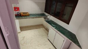 Una cocina pequeña y limpia con paredes blancas, encimera de mármol verde y ventana con marcos de madera.