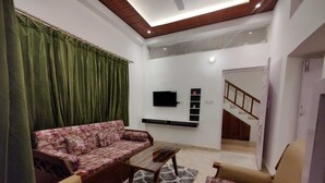 Salón con sofá, dos sillones, una mesa de centro, televisor de pantalla plana montado en la pared y una escalera que sube a otro nivel.