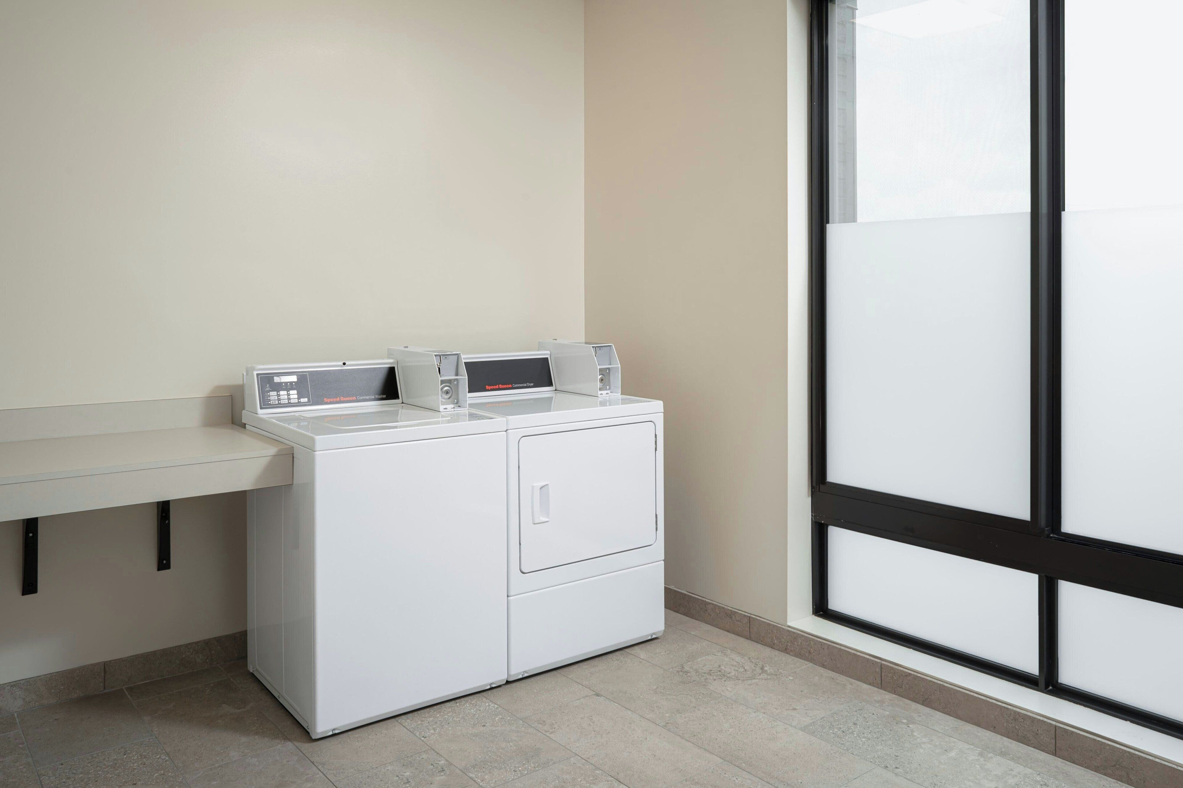 A laundry area with a washing machine and dryer, a countertop, and a large window.