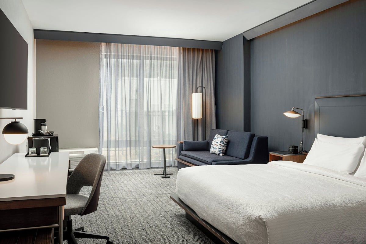 A modern hotel room with a large bed, a desk with a chair, a sofa, and a small table.