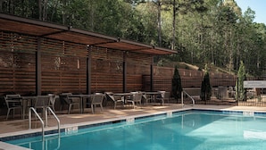 Une piscine avec une terrasse en bois et des chaises, entourée d’arbres.