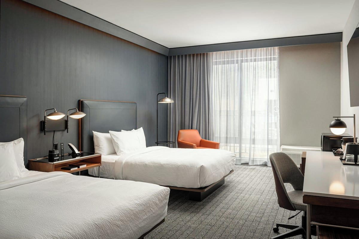 A hotel room with two beds, a desk, a chair, and a large window with curtains.