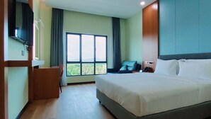 A hotel room with a large bed, a TV mounted on the wall, a desk, and a window with a view of greenery. - Hotel Kapalai (Semporna)