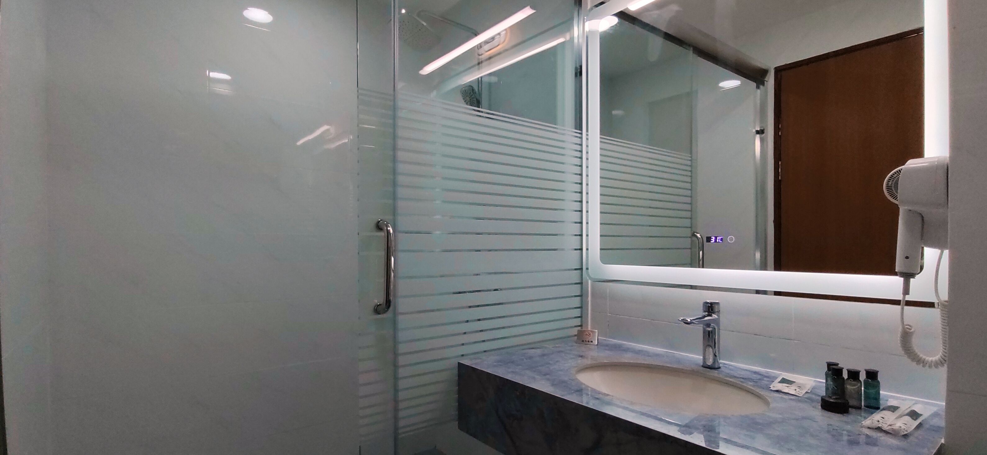 A modern bathroom with a glass shower enclosure, a marble sink, and a large mirror.