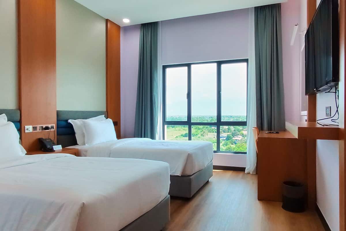 A hotel room with two beds, a large window, a TV, and a small desk.