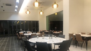 A spacious dining area with round tables and chairs, large windows, and hanging pendant lights. - Hotel Kapalai (Semporna)