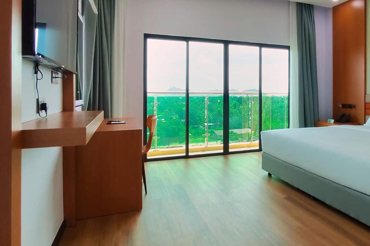 A hotel room with a large bed, a desk, and a balcony with a view of greenery.
