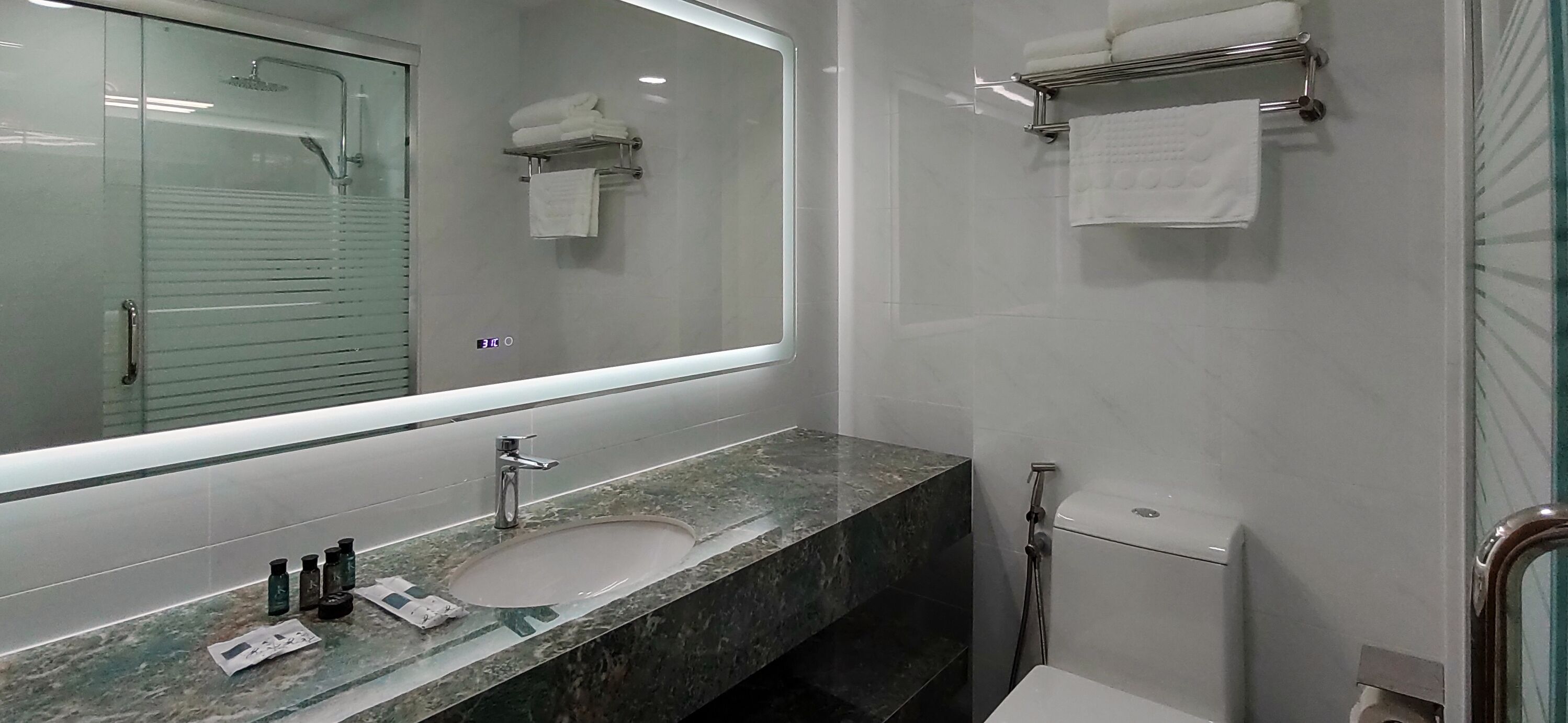 A modern bathroom with a large mirror, a sink with a marble countertop, and a glass shower enclosure.