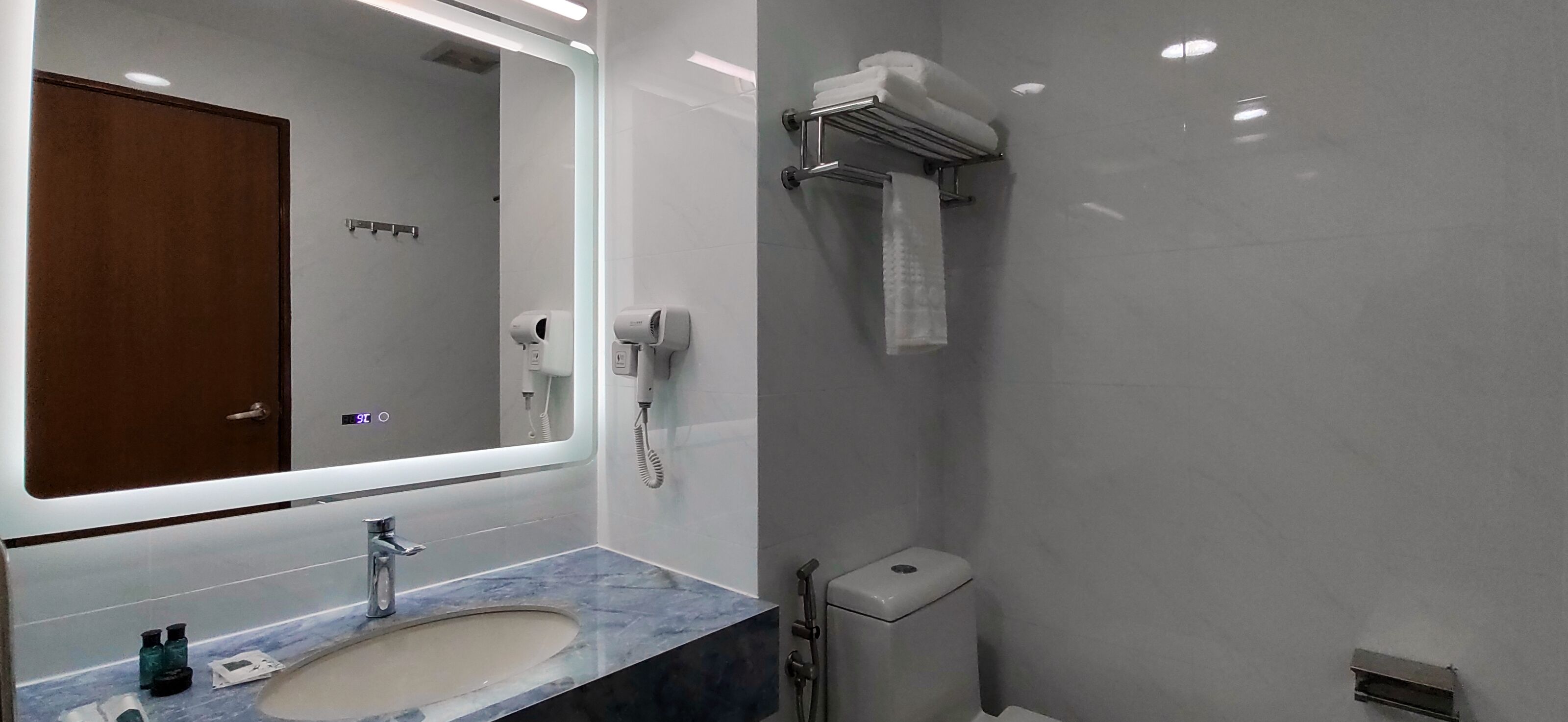 Une salle de bain moderne avec un lavabo en marbre, un miroir, un porte-serviettes, un sèche-mains et des toilettes.