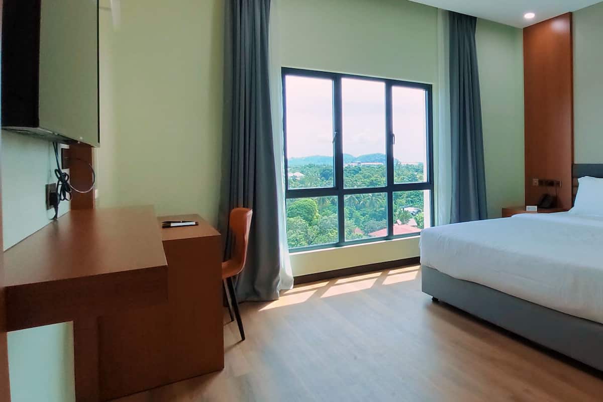 A hotel room with a large bed, a desk, and a view of greenery through a window.