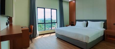 A hotel room with a large bed, a desk, and a view of greenery through a window.