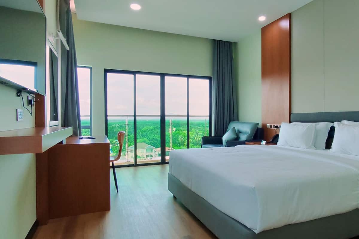 A modern hotel room with a large bed, a desk, and a chair. There is a large window with a view of the city.