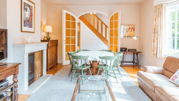 Un comedor con una mesa blanca y sillas verdes, una chimenea y una escalera que sube a otra habitación.