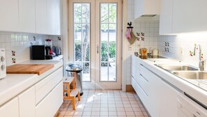Una cocina moderna con armarios blancos, una encimera de madera, una cafetera negra, un lavabo y una ventana con vistas a árboles.