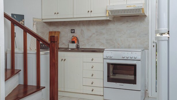 Una cocina con armarios blancos, una escalera de madera y un horno blanco.