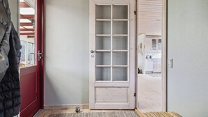 Eine Tür mit Fensterglas, eine rote Tür links und eine Bank im Vordergrund.