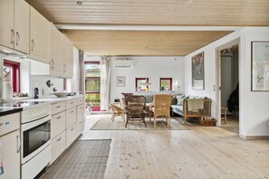A modern kitchen with wooden cabinets, a dining area with wicker furniture, and a view of greenery outside.