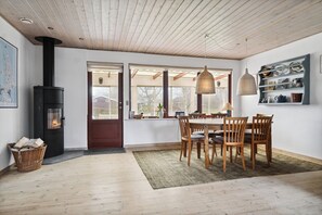A dining area with a wooden table and chairs, a black wood-burning stove, and a window with a view.
