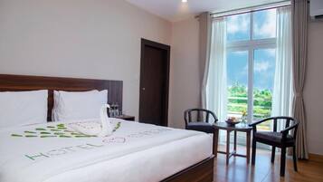 A hotel room with a large bed, a wooden headboard, a small table with chairs, and a window with curtains.