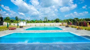 A rectangular swimming pool with a tiled deck, surrounded by outdoor seating and greenery. - Hotel Orion (Sunwal)