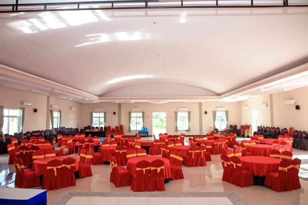 A large hall with multiple round tables covered in red tablecloths and yellow sashes, arranged in a circular pattern.