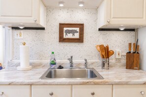 A kitchen with a marble countertop, stainless steel sink, wooden utensils, and a framed picture on the wall. - Fun Designer space with Patio! (Pittsburgh)