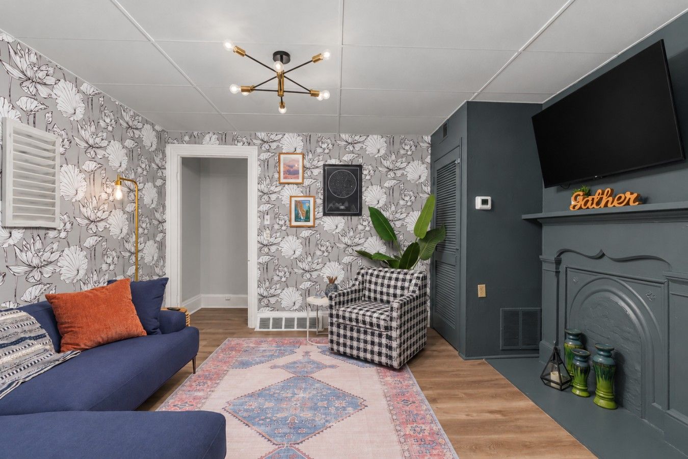 A living room with a blue sofa, patterned rug, checkered chair, and a fireplace with a 'Father' sign.