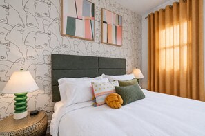 A neatly made bed with pillows and a headboard, two bedside lamps, and a patterned wall. - Fun Designer space with Patio! (Pittsburgh)