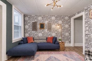 A room with a dark blue sofa, patterned wallpaper, a floor lamp, and a patterned rug. - Fun Designer space with Patio! (Pittsburgh)