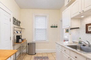 A kitchen with white cabinets, a stainless steel sink, a coffee maker, and a trash can. - Fun Designer space with Patio! (Pittsburgh)