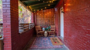 Un espace de détente extérieur accueillant, avec un mur en briques, des chaises en bois, une table et un tapis décoratif.