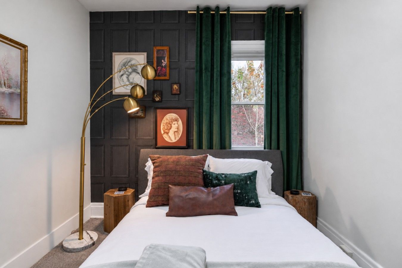 A bedroom with a bed, a floor lamp, and artwork on the wall.
