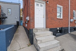 A residential building with a white door, a brick facade, and a concrete staircase leading to the entrance. - Fun Designer space with Patio! (Pittsburgh)