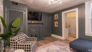 Un salon avec un canapé à carreaux, un téléviseur placé au-dessus d’une cheminée et un banc bleu.