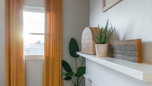 Une pièce avec une fenêtre, une plante en pot, une étagère ornée d’objets décoratifs et un rideau.