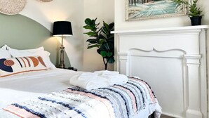 A neatly made bed with a striped blanket, a bedside lamp, a framed painting, and a potted plant.