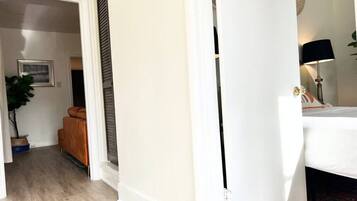 A hallway with a white door, a bed with a black headboard, a lamp, and a plant.