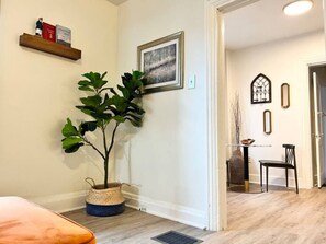 Ein Zimmer mit Blumentopf, einem gerahmten Bild, einem Bücherregal und einer Essecke mit Stuhl und Tisch.