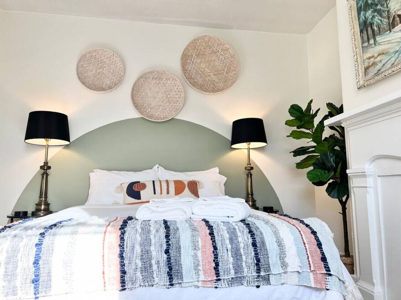 A neatly made bed with a striped blanket, two lamps, and three wall-mounted round decorations.