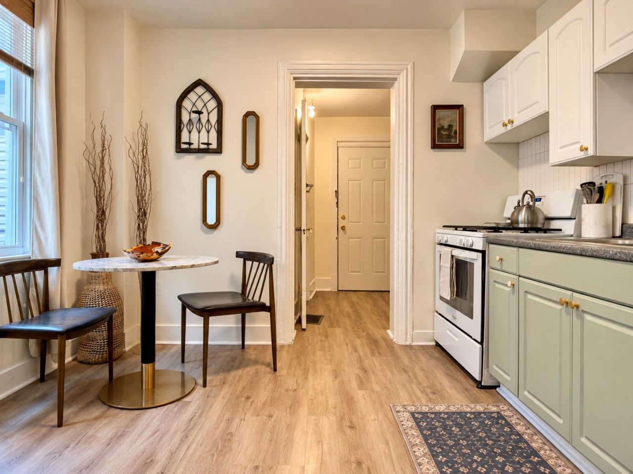 Een keuken met een fornuis, oven en kasten. Er is een eethoek met een tafel en stoelen.