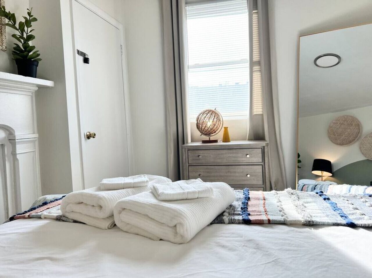 A neatly made bed with folded towels, a bedside table with a lamp, and a mirror on the wall.